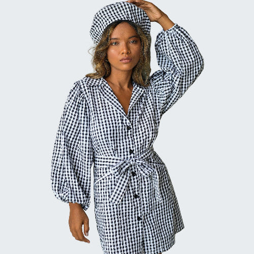 Woman wearing a black and white checkered dress and hat against a plain background