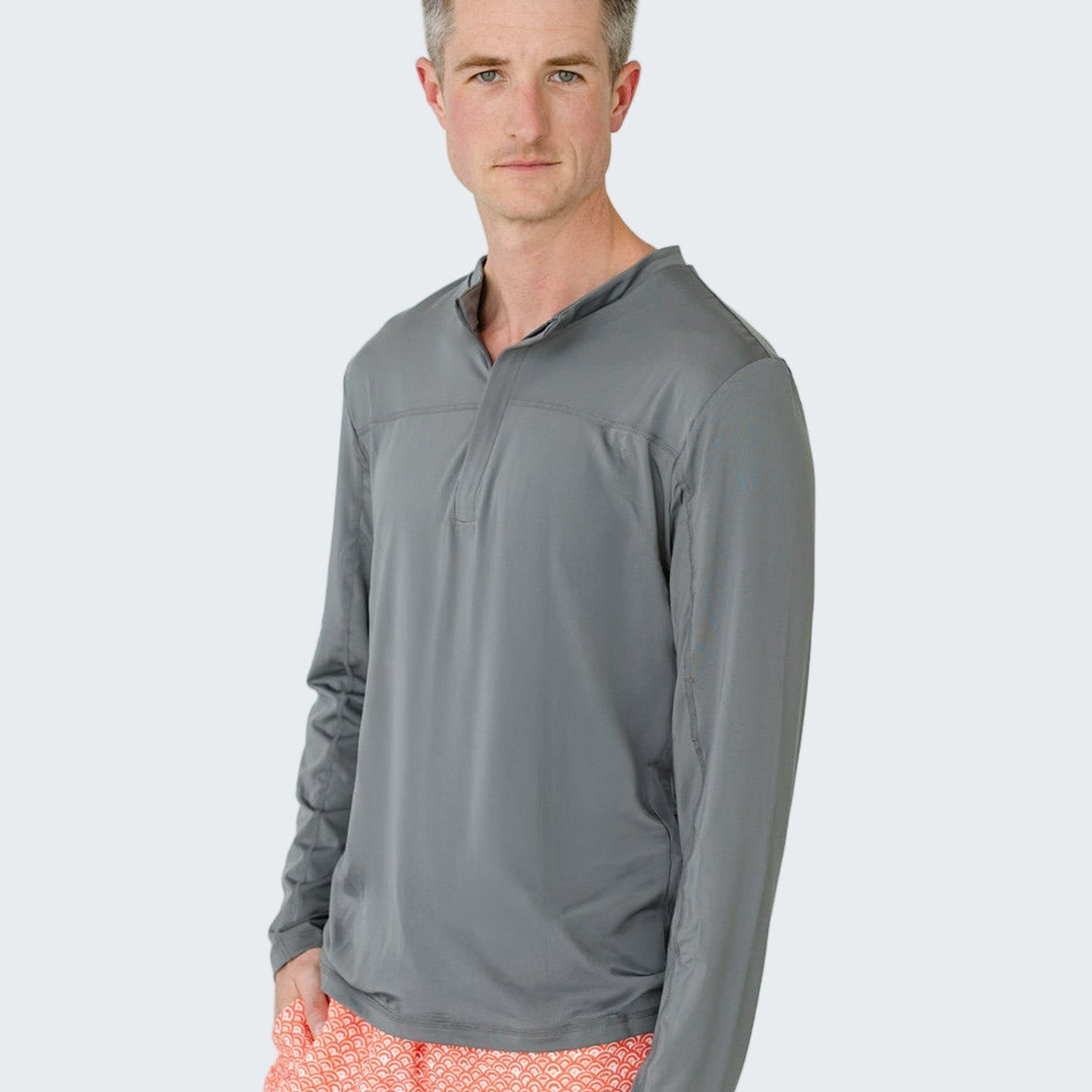 Man wearing a gray long-sleeve shirt and pink shorts with a white pattern on a light gray background
