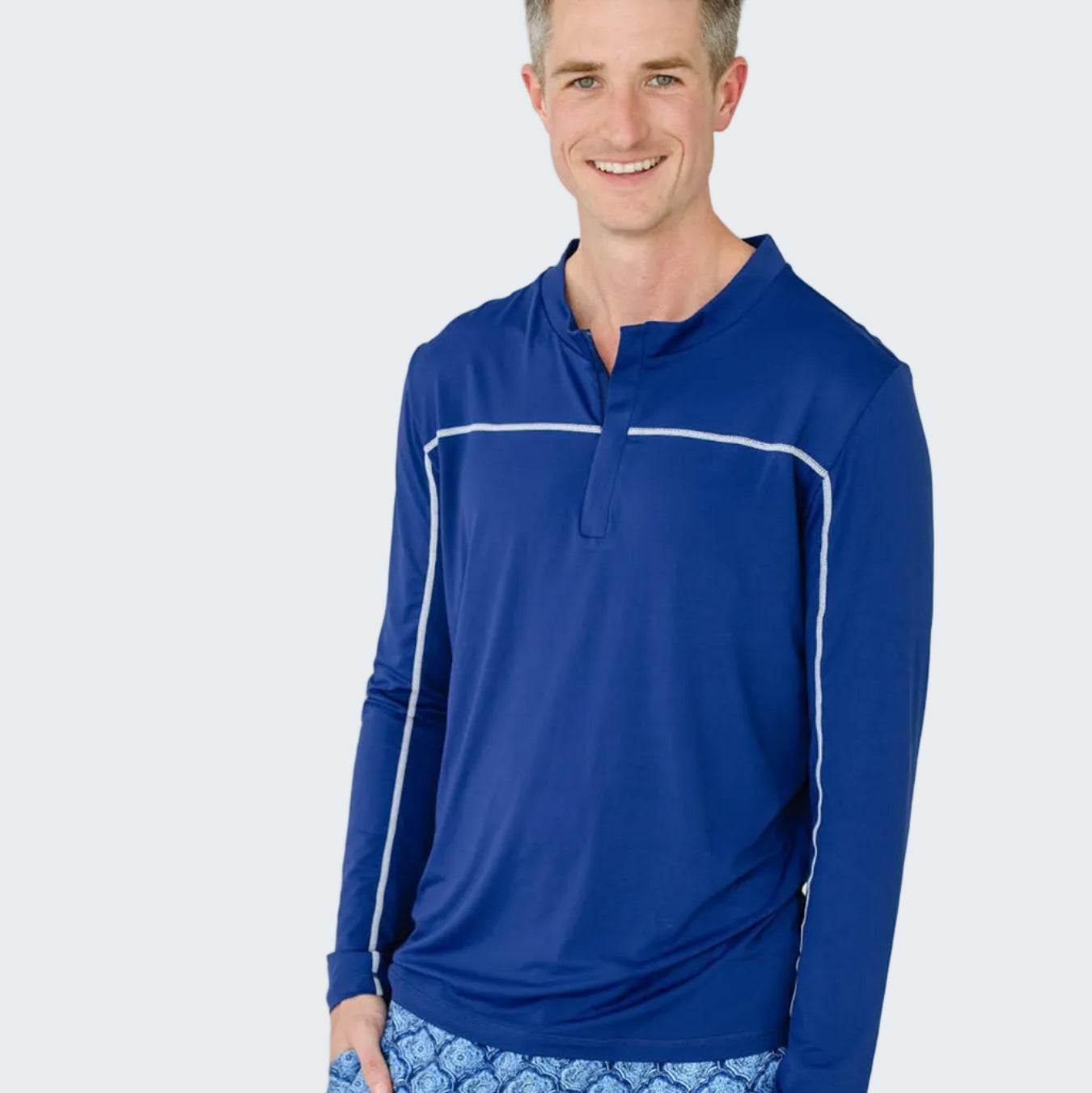 Man wearing a blue long-sleeve shirt and patterned shorts on a white background