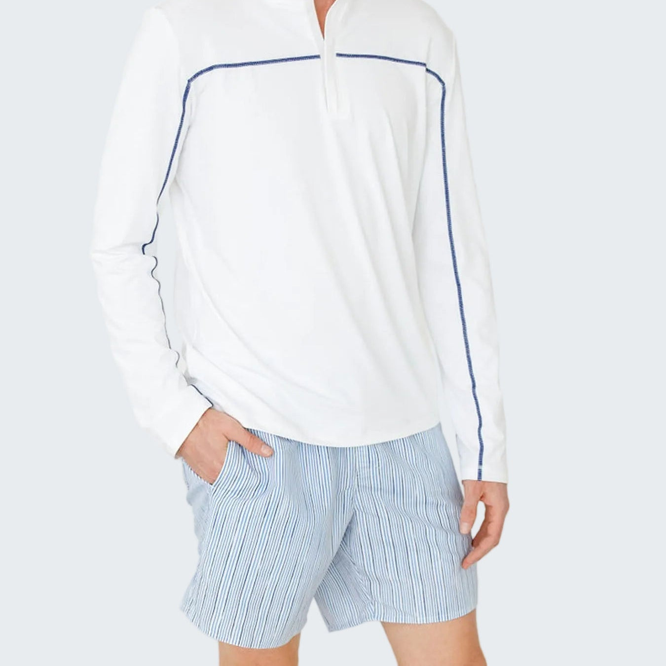 Man wearing a white long-sleeve shirt with blue accents and light blue shorts on a white background