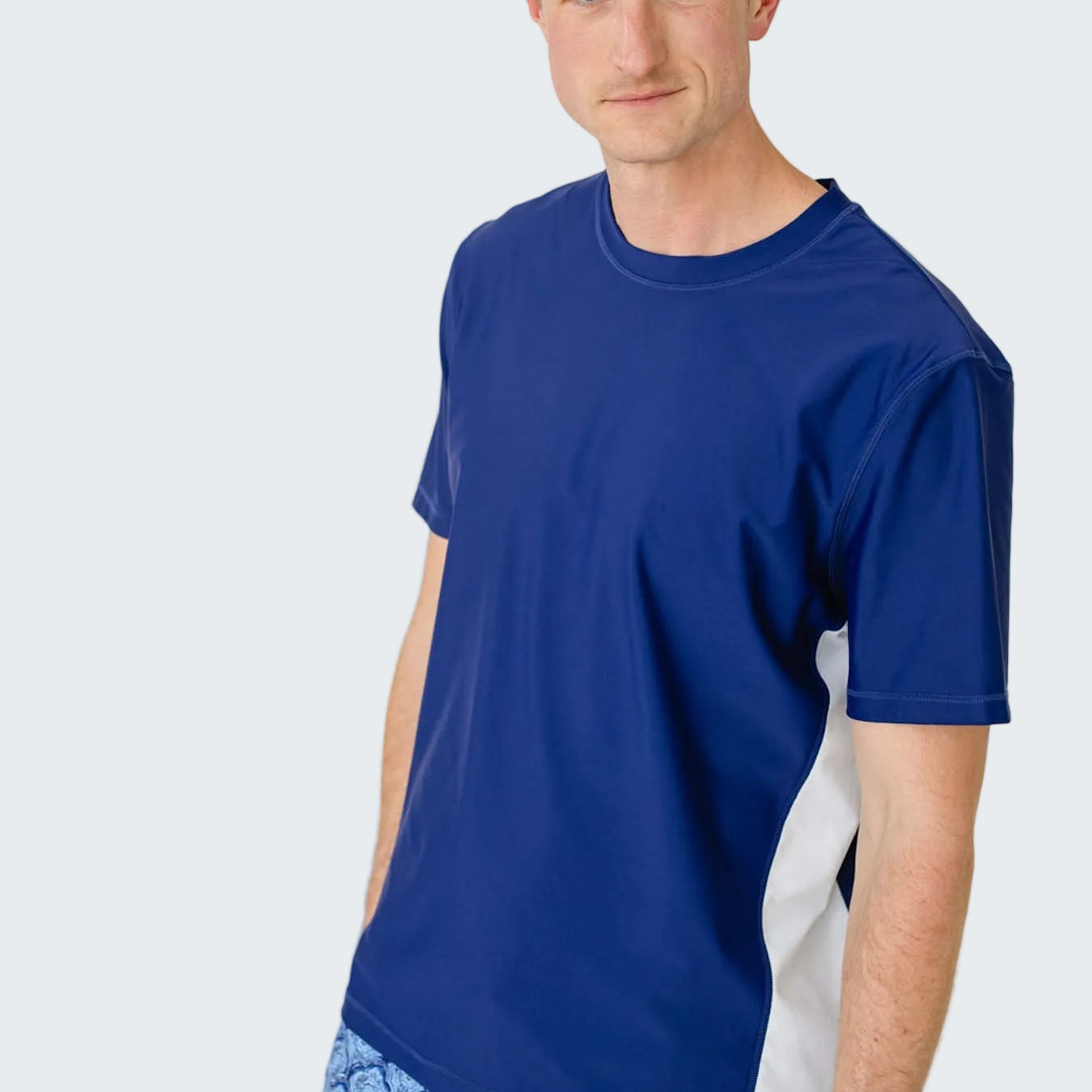 Man wearing a blue t-shirt and patterned shorts on a white background