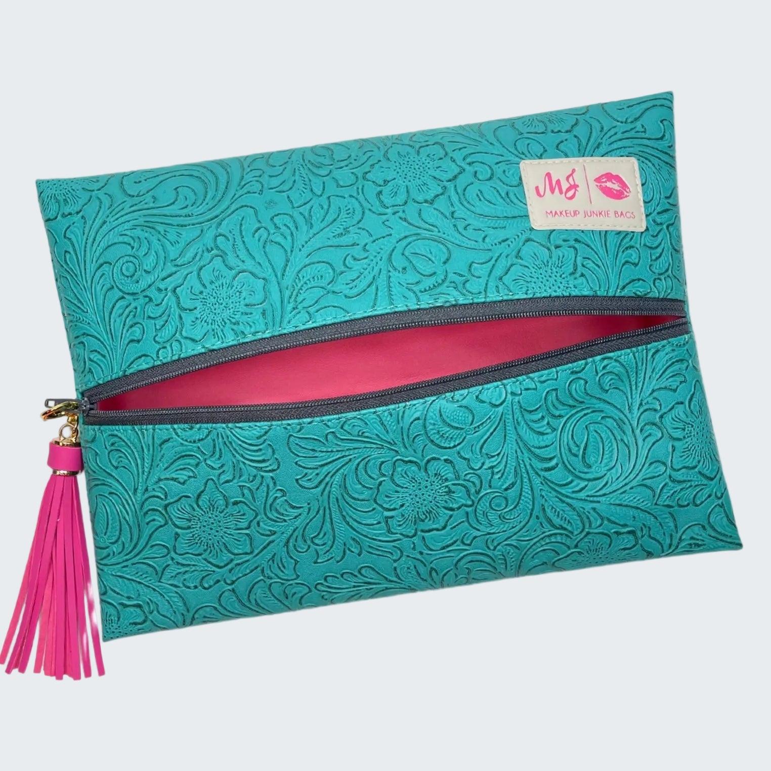 Teal patterned clutch with pink interior and tassel on a white background
