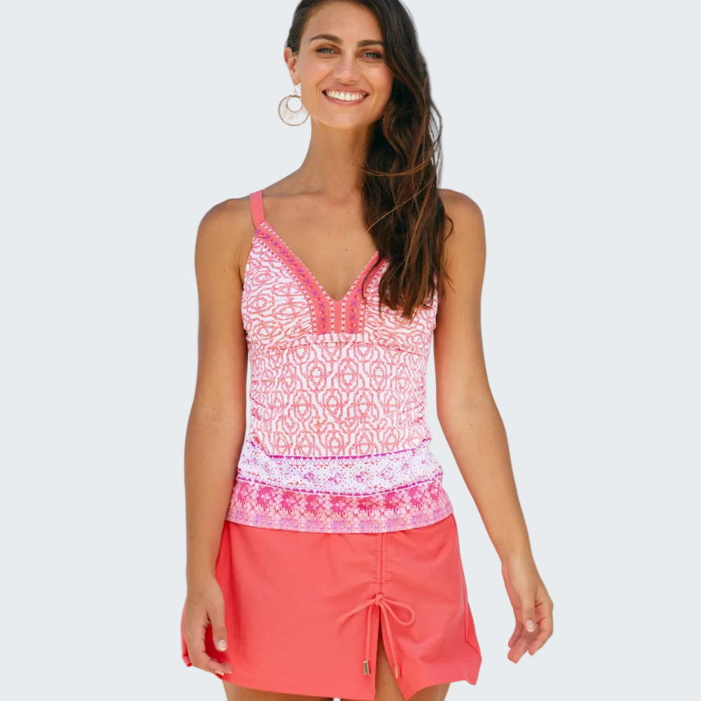 Woman wearing a pink patterned top and coral skirt on a beach