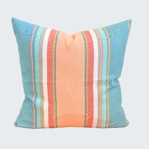 Striped pillow with blue, orange, and white colors on a wooden stool.