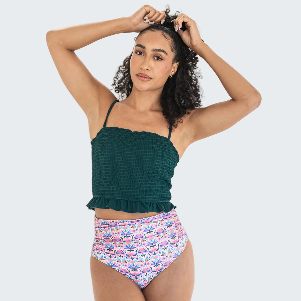 Woman wearing a green top and floral high-waisted bikini bottom on a white background