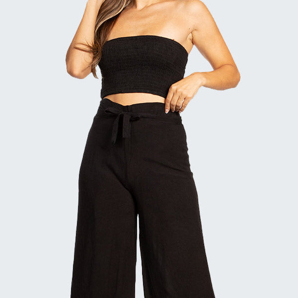 Woman wearing a black strapless top and wide-leg pants on a white background