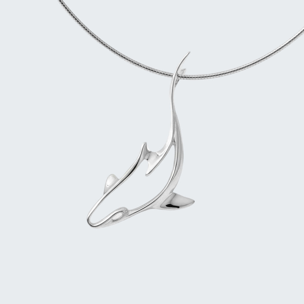 Silver dolphin pendant on a chain against a white satin background