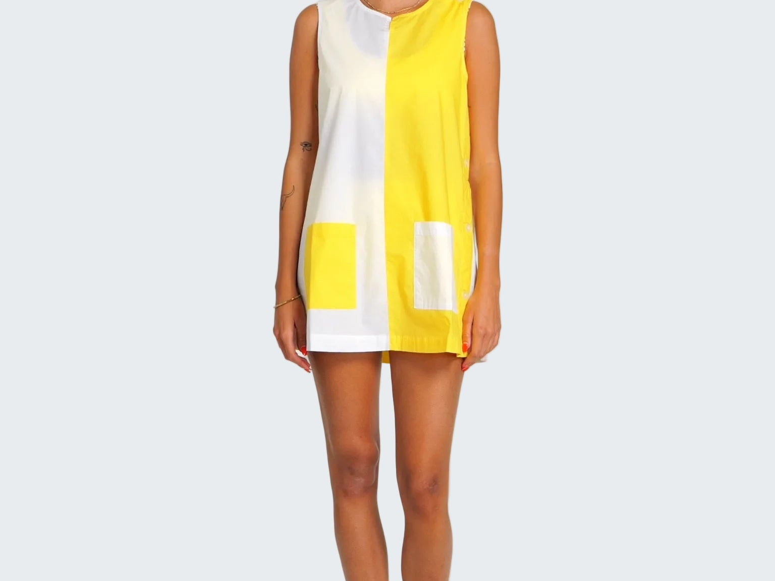 Woman wearing a yellow and white sleeveless dress on a plain background