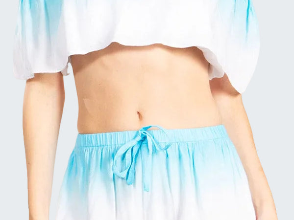 Woman wearing a blue and white gradient off-shoulder top and shorts set on a white background