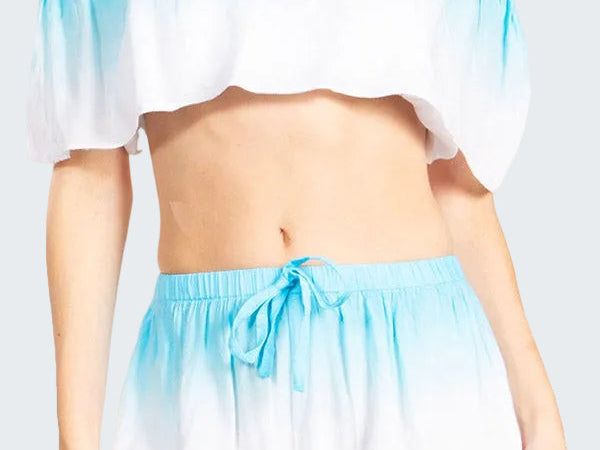 Woman wearing a blue and white gradient off-shoulder top and shorts set on a white background