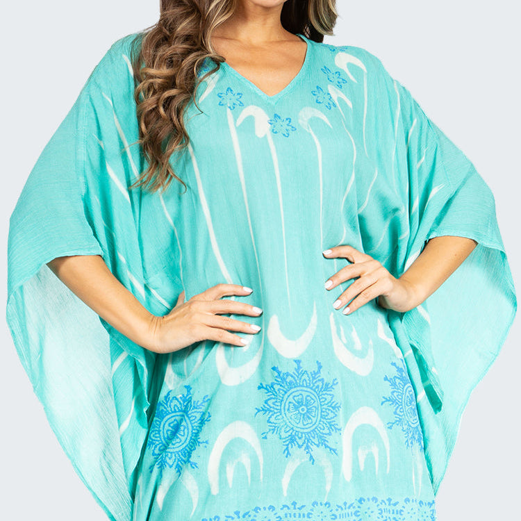 Turquoise poncho with white patterns worn by a person on a white background