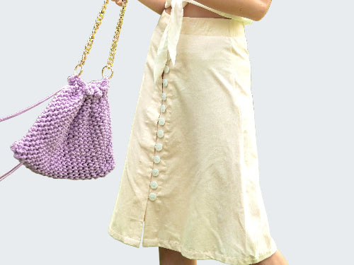 Person holding a purple beaded handbag with a blurred green outdoor background