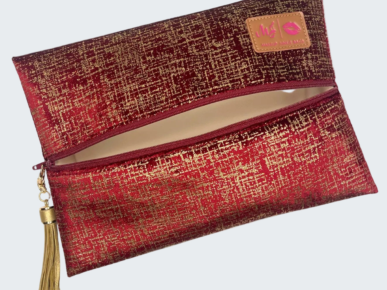 Red and gold patterned clutch bag with a tassel on a white background