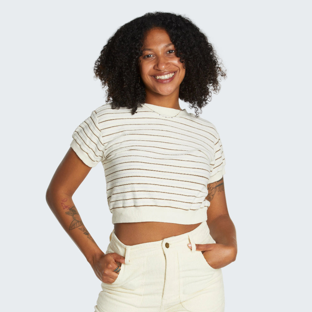Woman wearing a striped crop top and high-waisted pants against a plain background