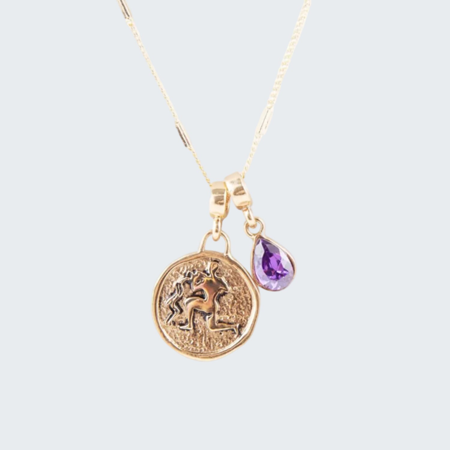 Gold necklace with a unicorn pendant and purple teardrop charm on a white background