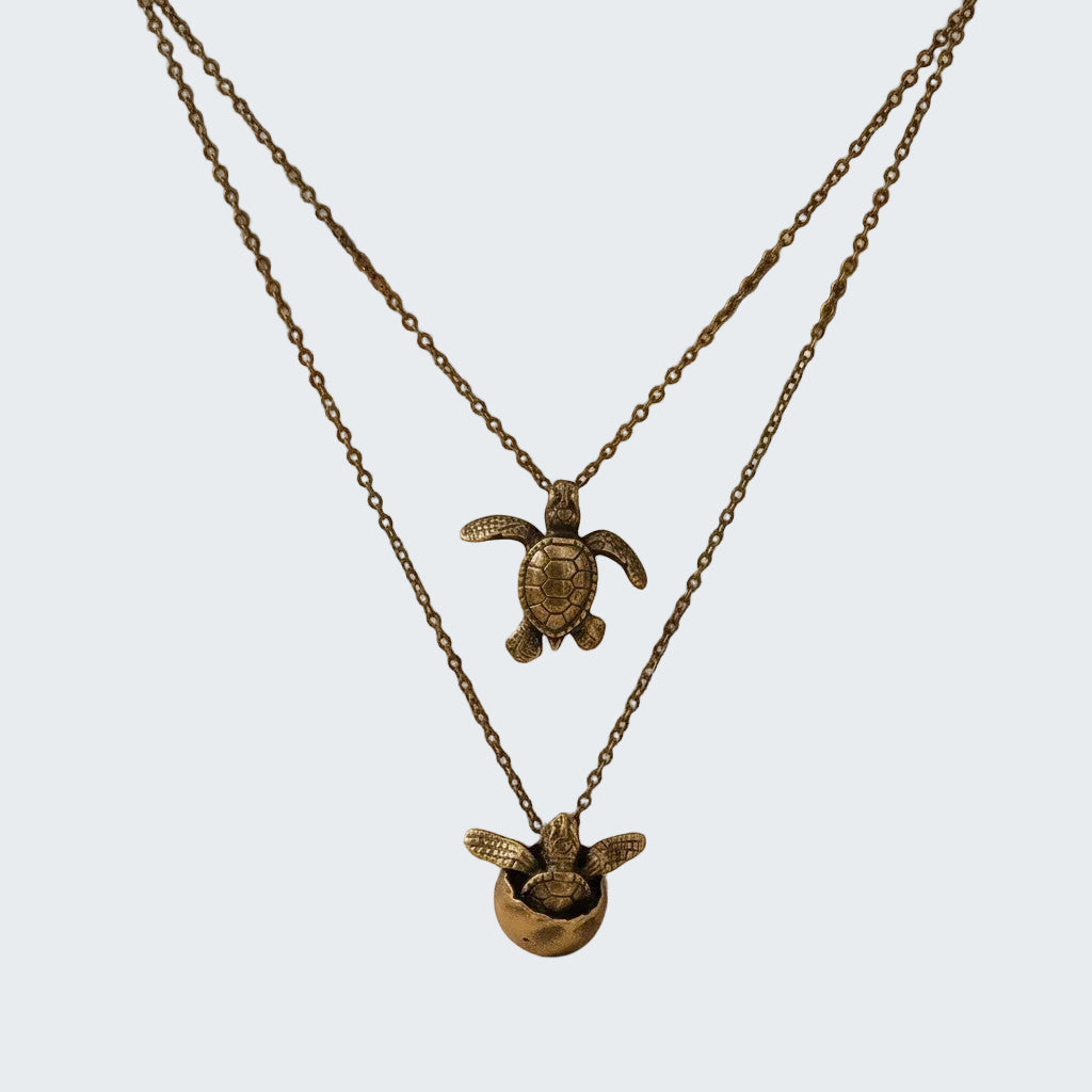 Two bronze turtle necklaces on a beige fabric background