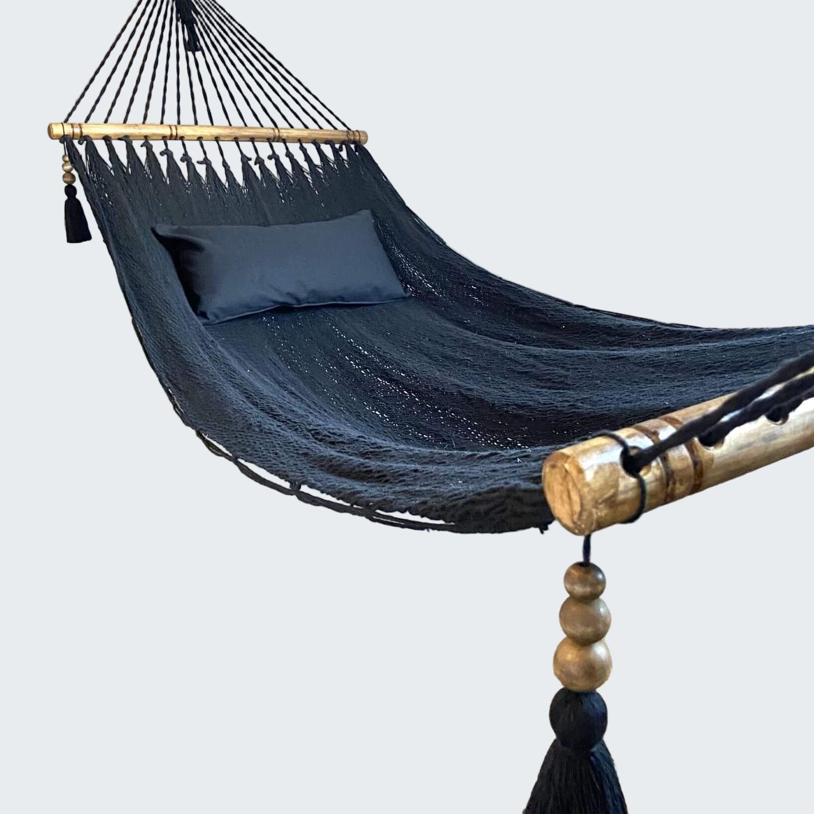 Navy blue hammock with wooden poles and tassels in a room with a textured rug and decorative wall.