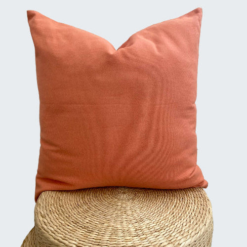 Coral pillow on a woven stool with a decorative white lattice background