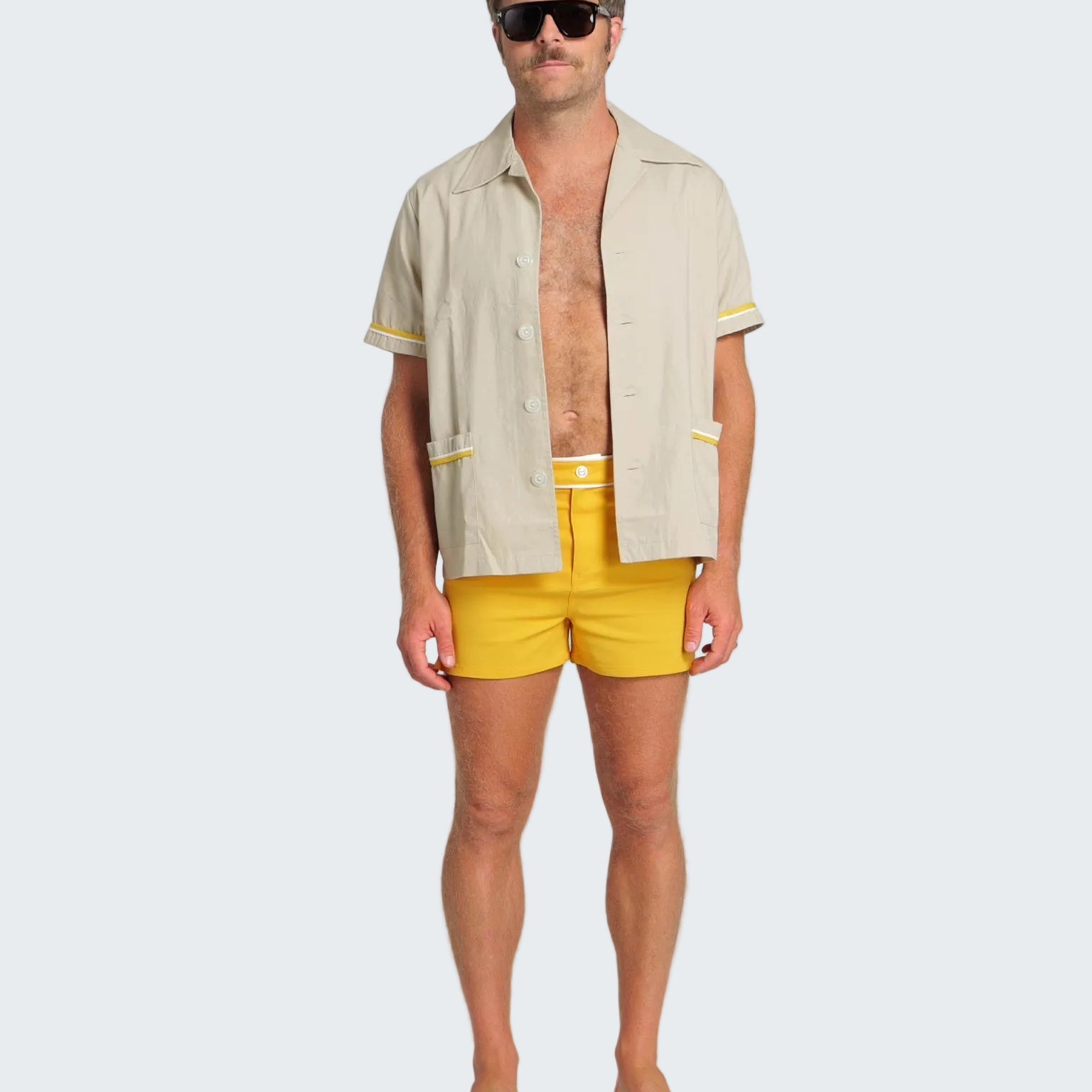 Man wearing a beige shirt with yellow trim and yellow swim shorts on a white background