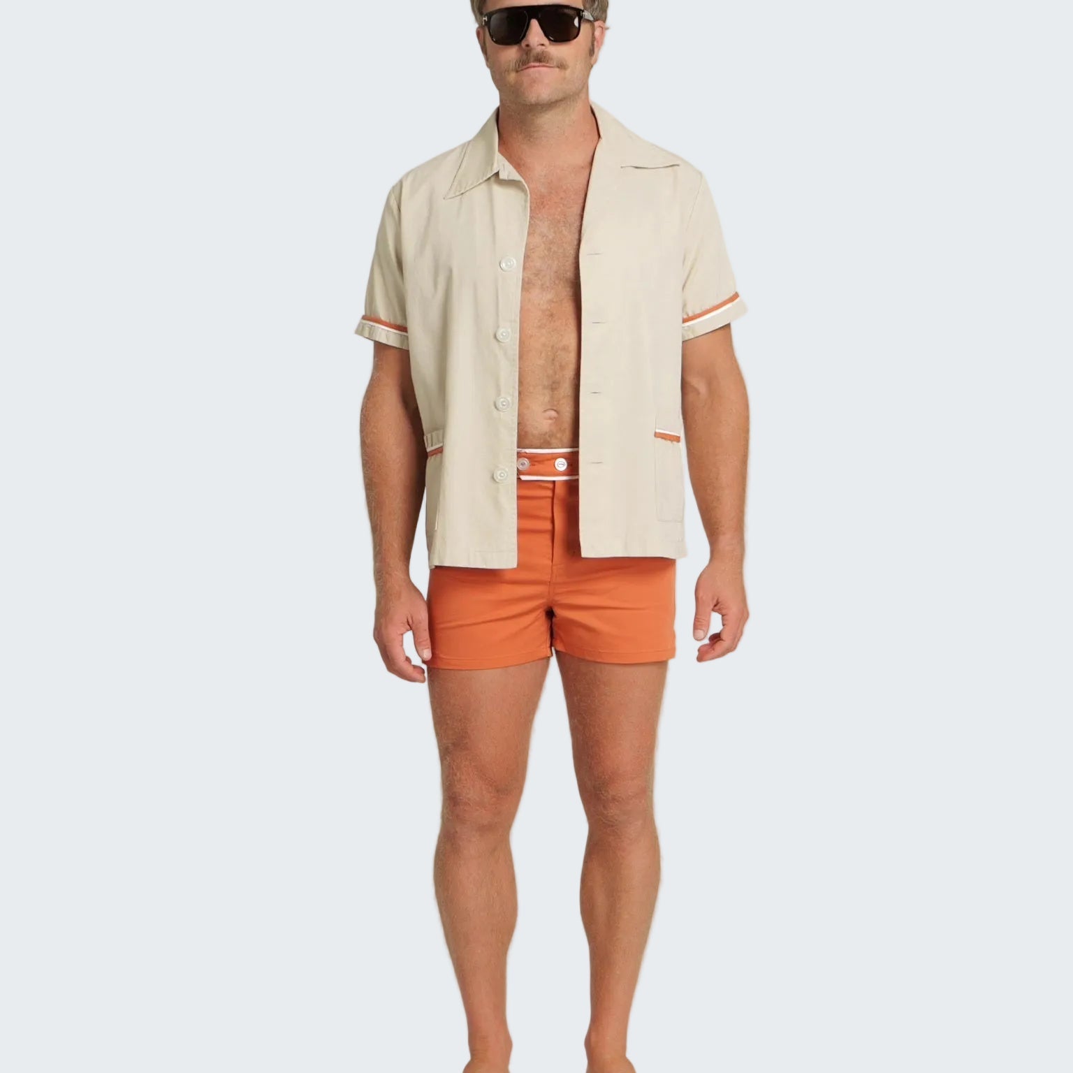 Man wearing a beige shirt and orange swim shorts on a white background
