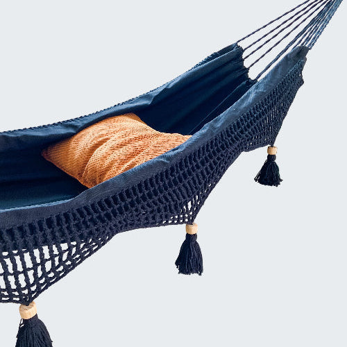 Navy blue hammock with orange pillow in a room with a plant and window.