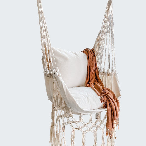 Macrame hammock chair with white cushion and brown blanket in a room with a white screen partition and plants.