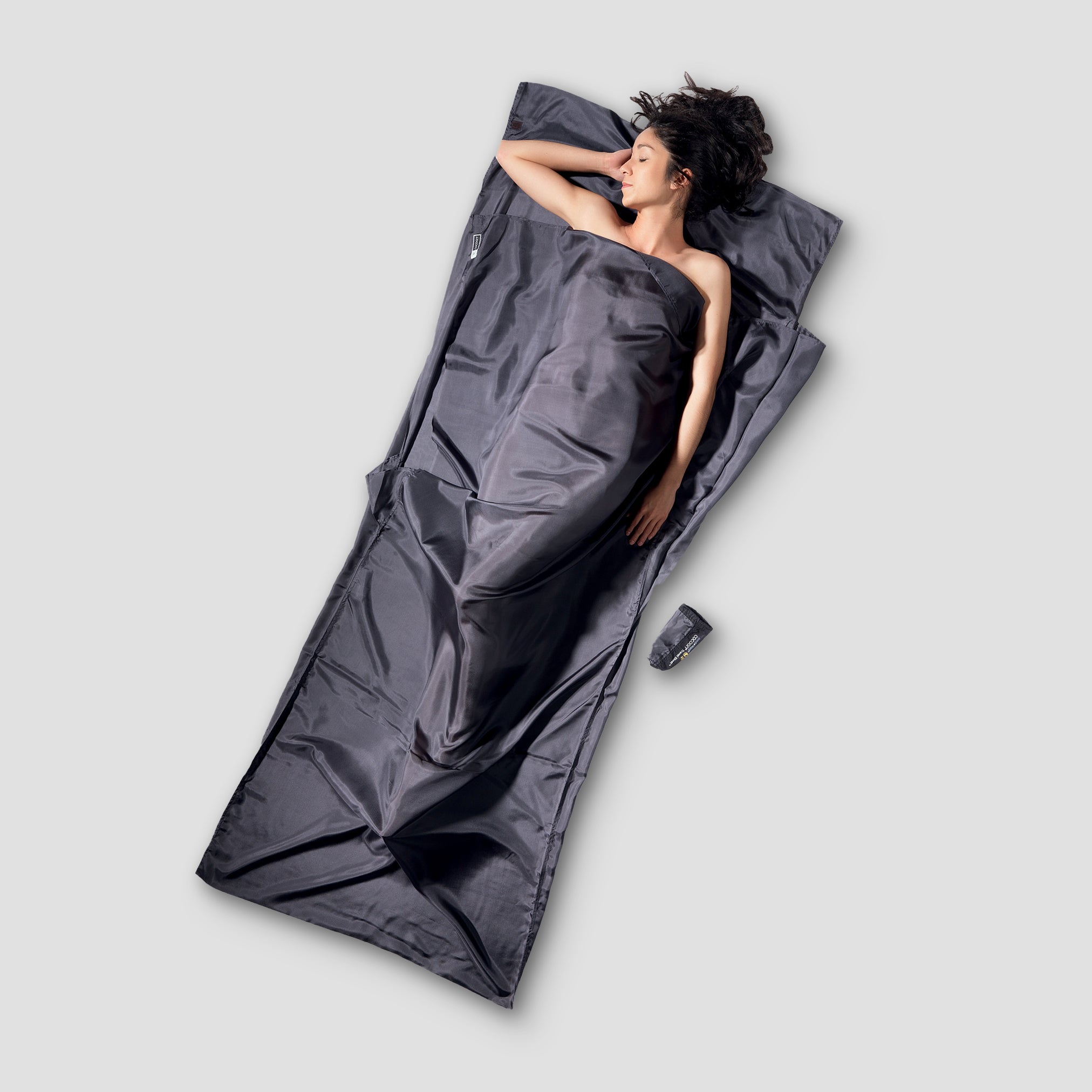 Person lying in a gray sleeping bag on a light gray background