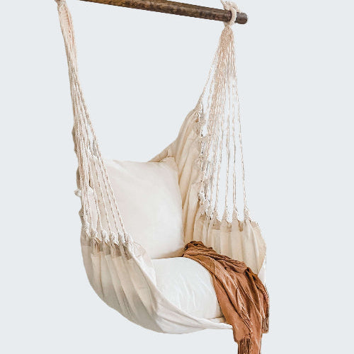 White hammock chair with a blanket in a room with a textured white wall and plant.