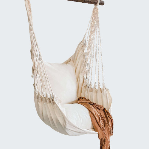 White hammock chair with a blanket in a room with a textured white wall and plant.