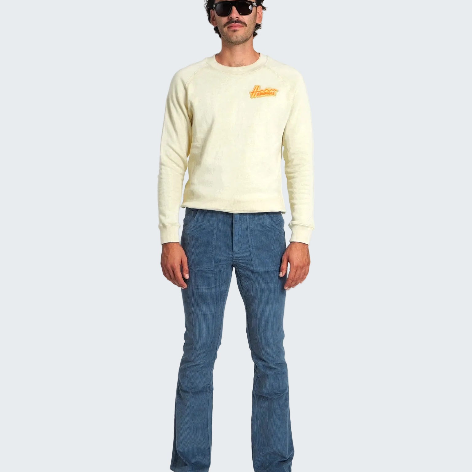 Man wearing a light-colored sweater and blue jeans on a white background