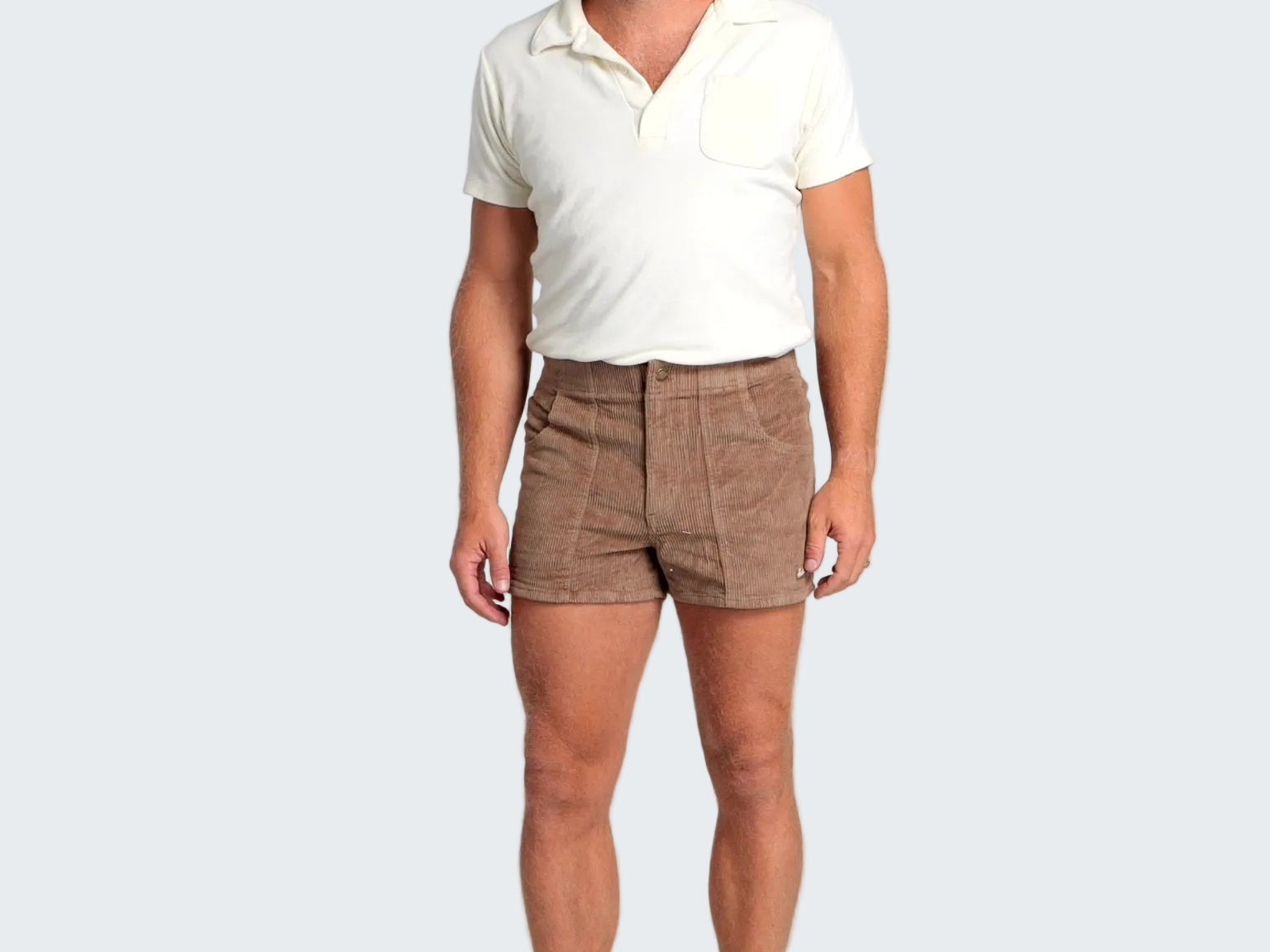 Man wearing a white polo shirt and brown shorts on a plain background