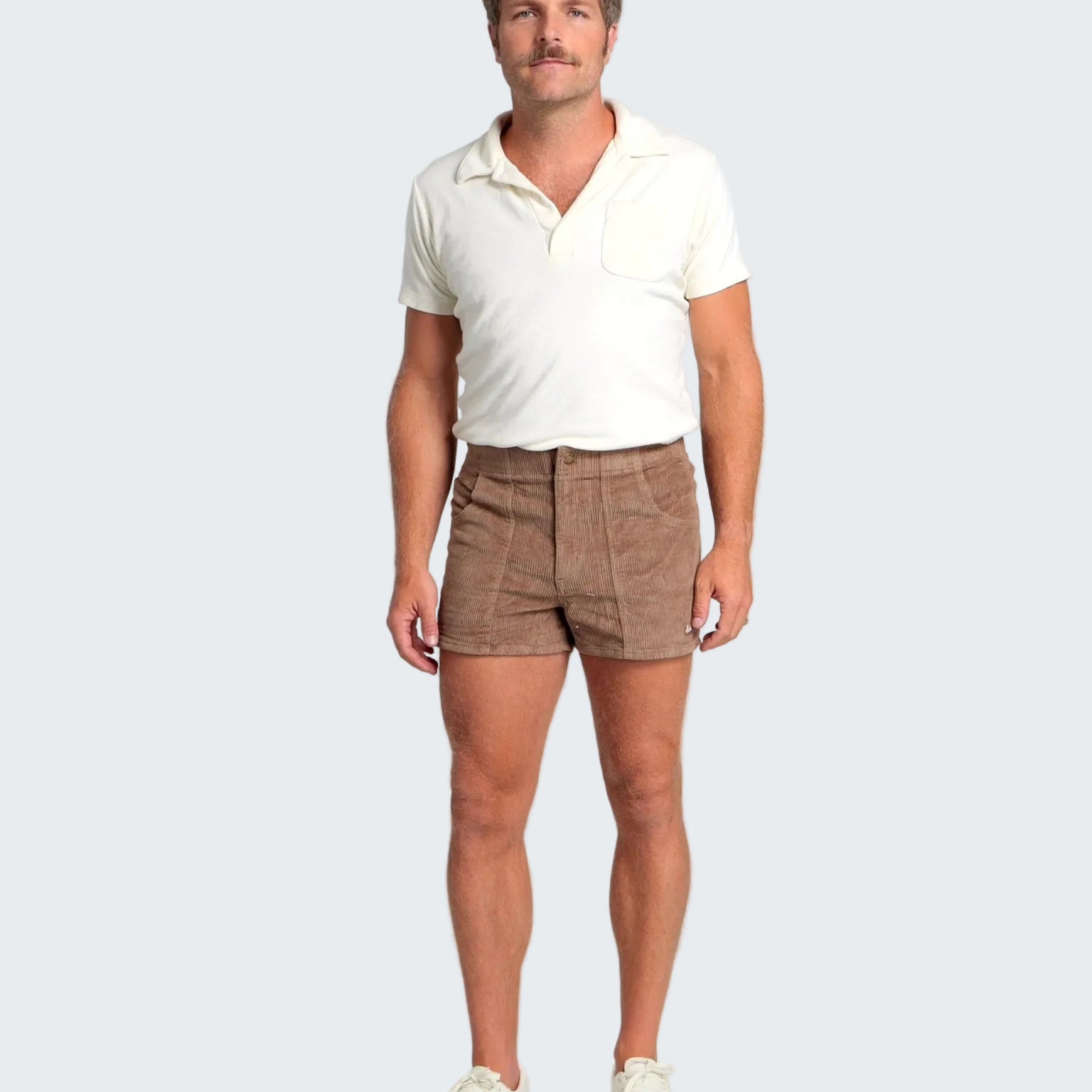 Man wearing a white polo shirt and brown shorts on a plain background