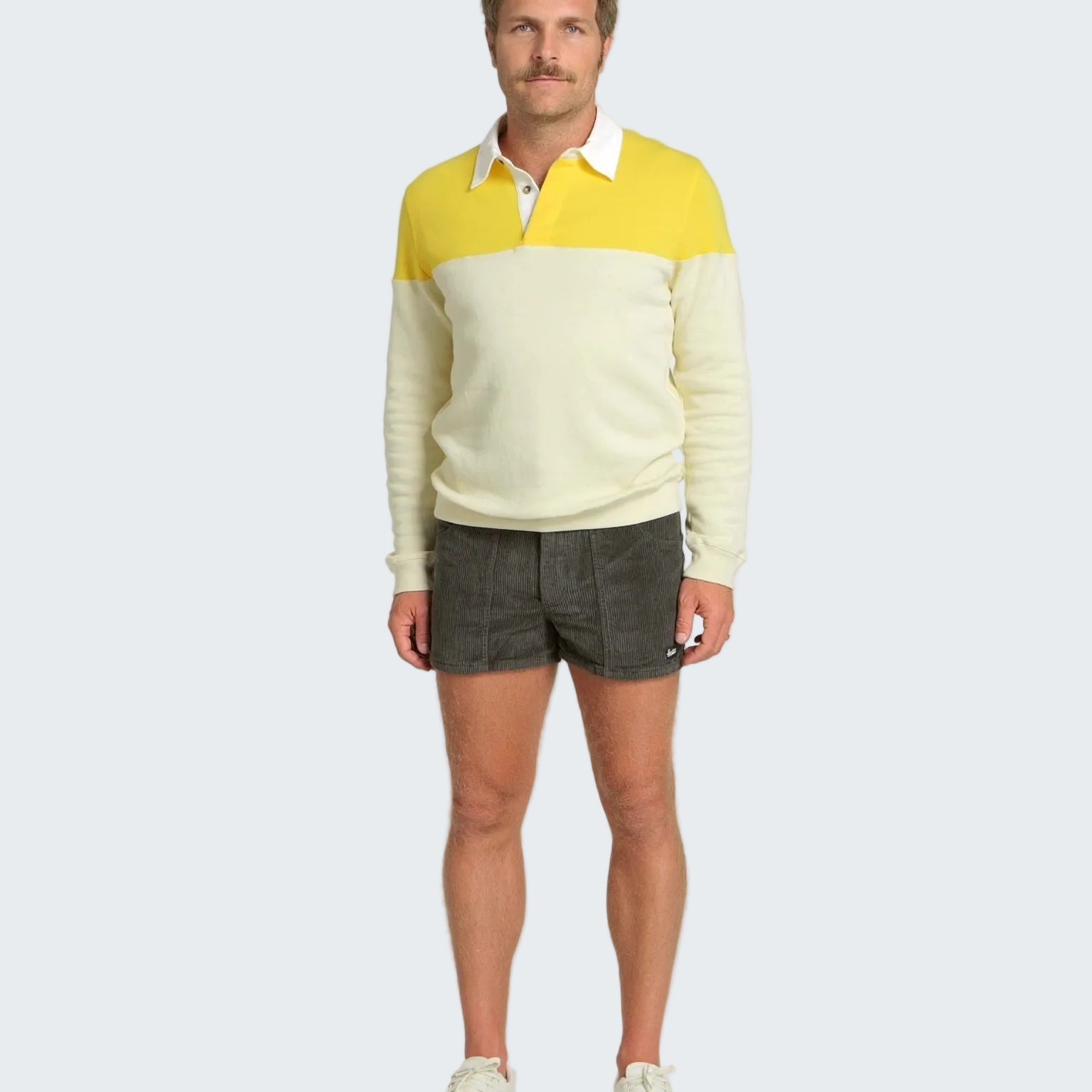 Man wearing a two-tone sweater with yellow and white, paired with dark shorts on a white background