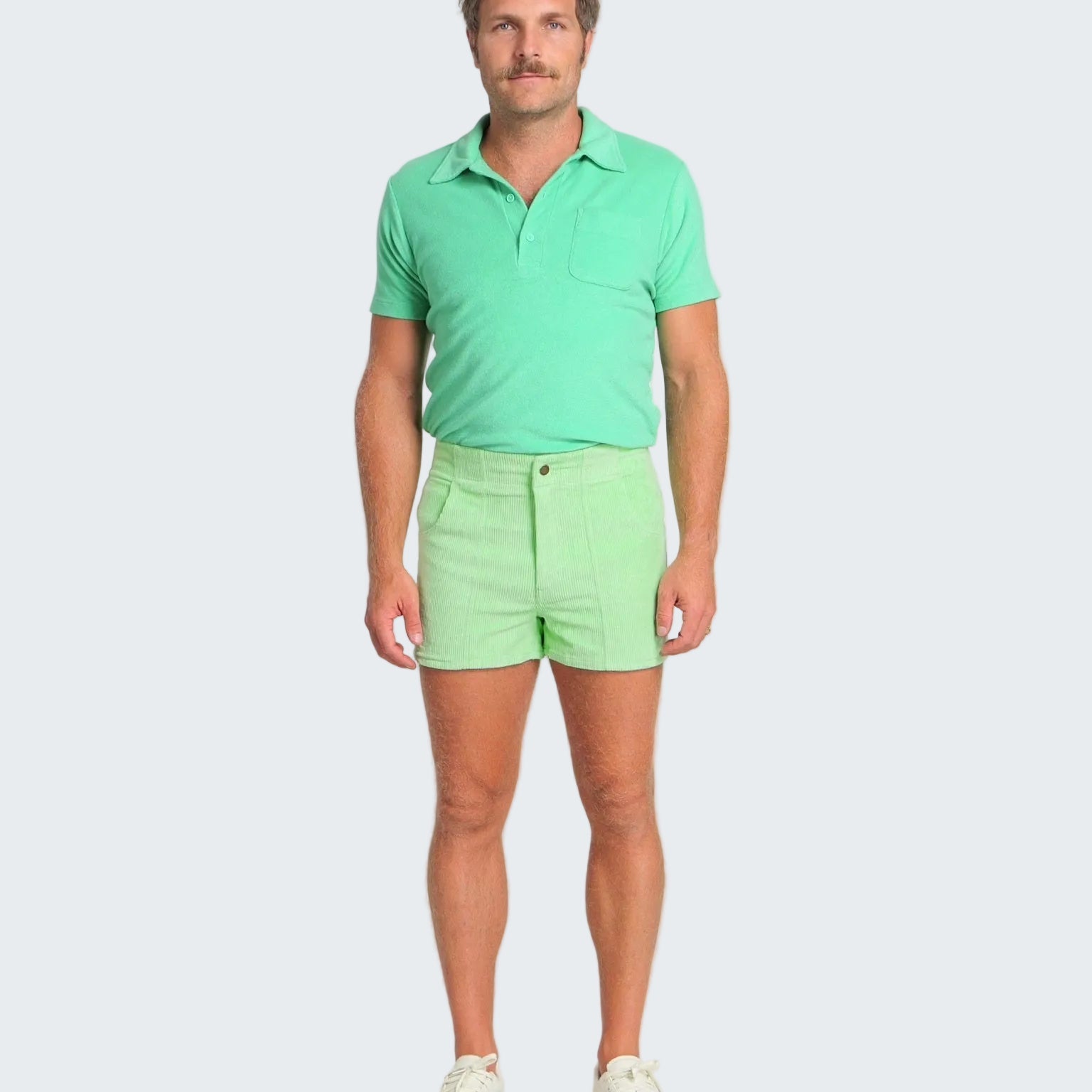 Man wearing a green polo shirt and shorts on a white background