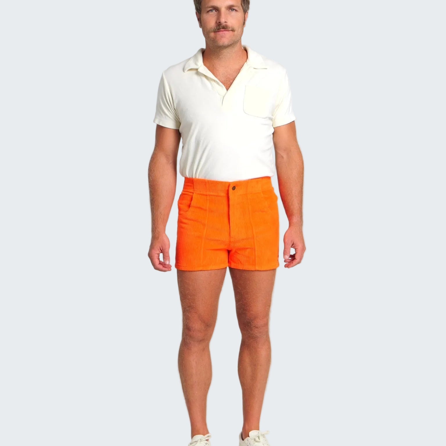 Man wearing a white polo shirt and bright orange shorts on a white background