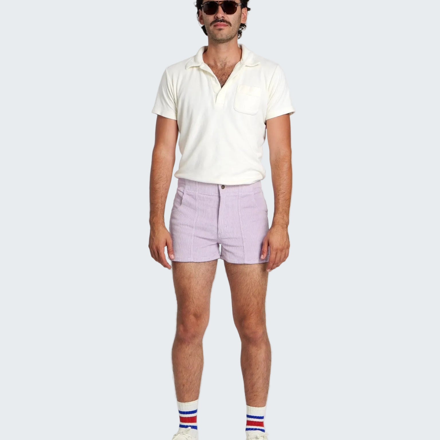 Man wearing a white polo shirt, light purple shorts, and striped socks on a white background
