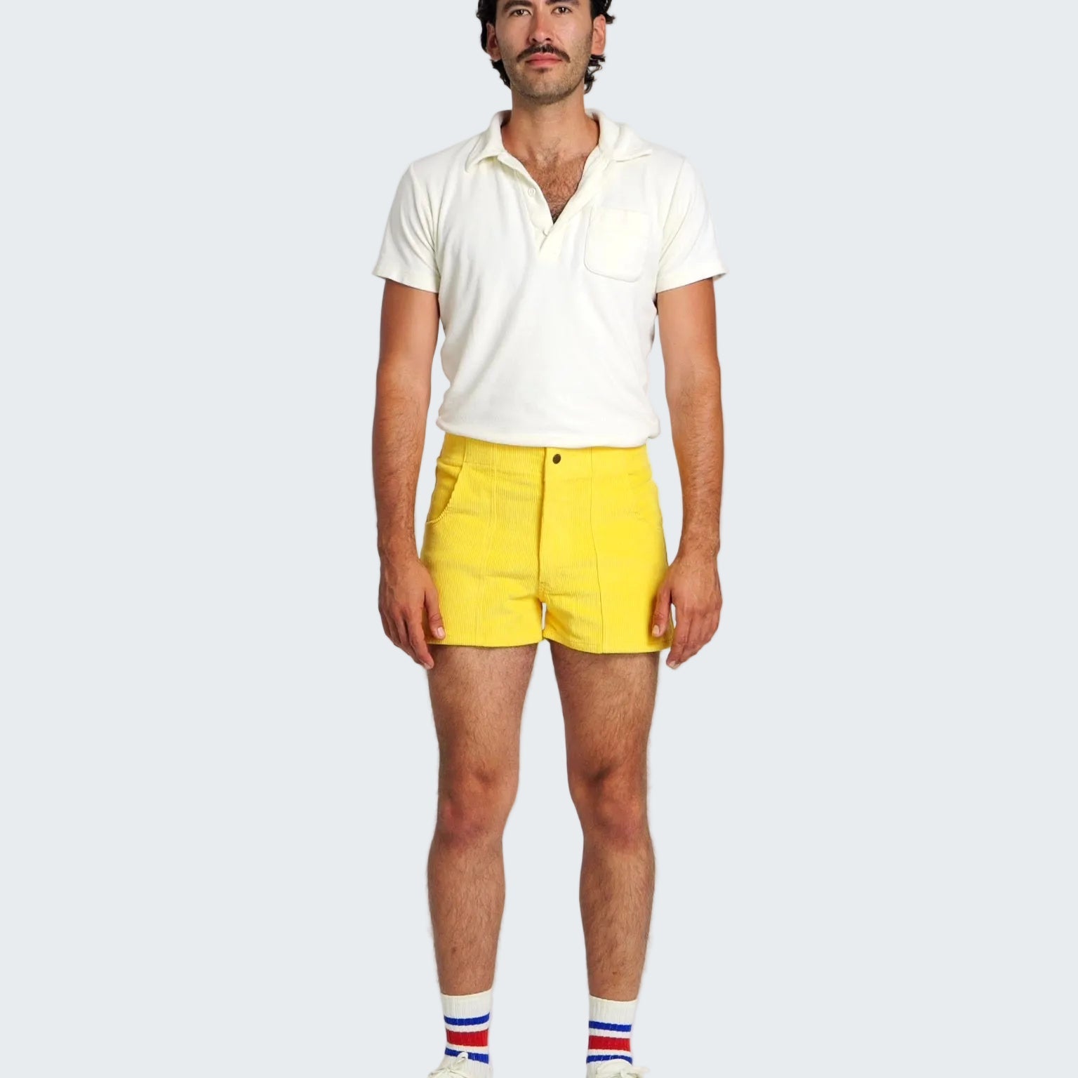 Man wearing a white polo shirt and yellow shorts with a plain background