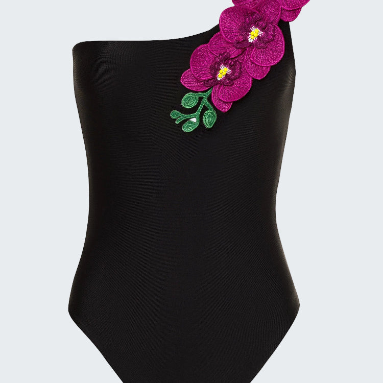 Black one-shoulder swimsuit with pink floral embellishments on a white background