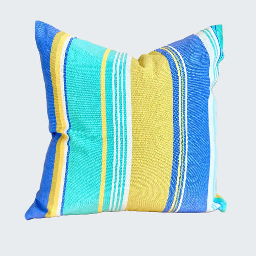 Striped pillow with blue, yellow, and white colors on a wooden stool against a beige wall.