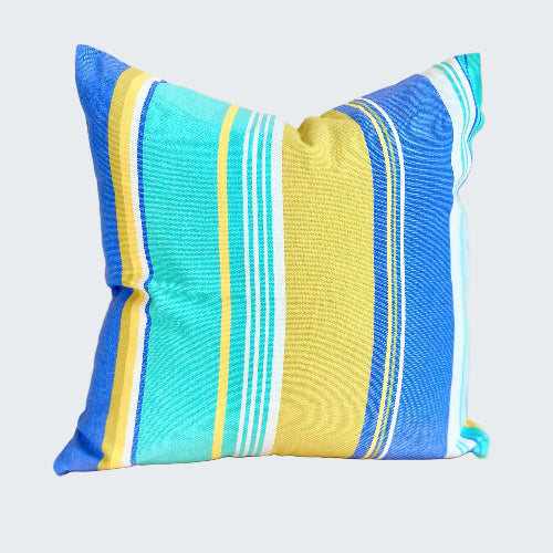 Striped pillow with blue, yellow, and white colors on a wooden stool against a beige wall.