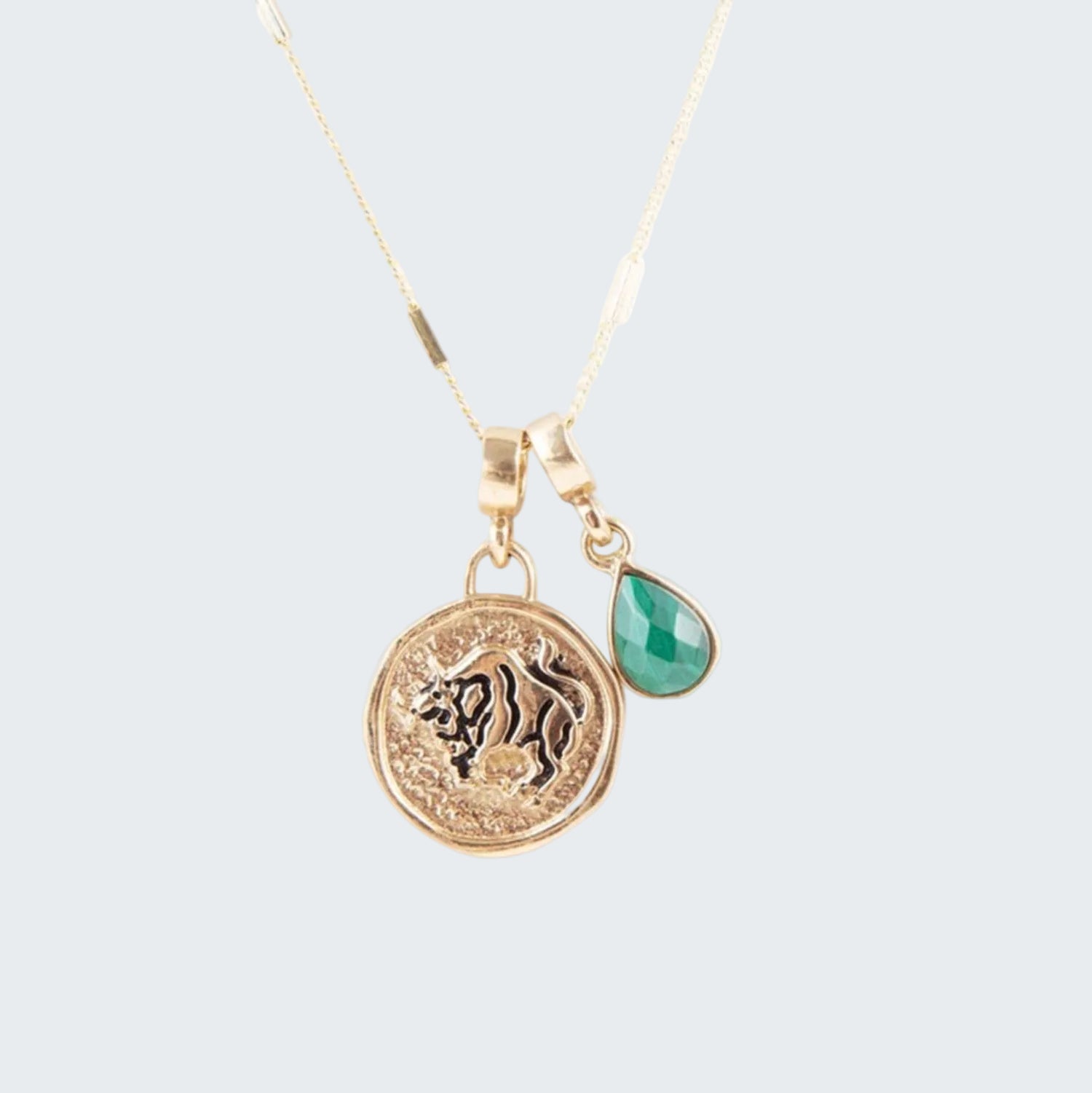 Gold necklace with lion emblem and green teardrop pendant on a white background