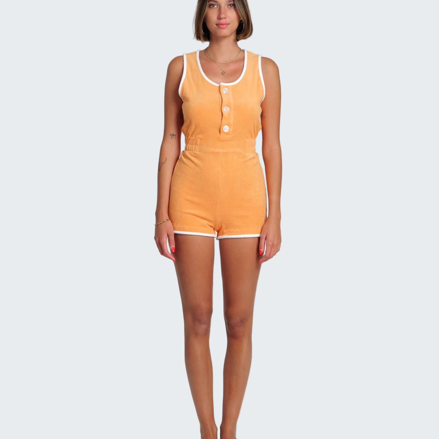 Woman wearing an orange romper with white trim on a white background