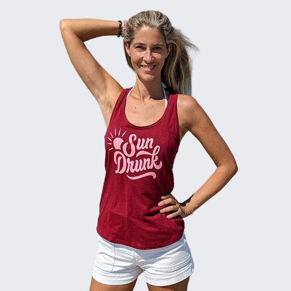 Woman wearing a red tank top with 'Sun Drunk' text on a beach