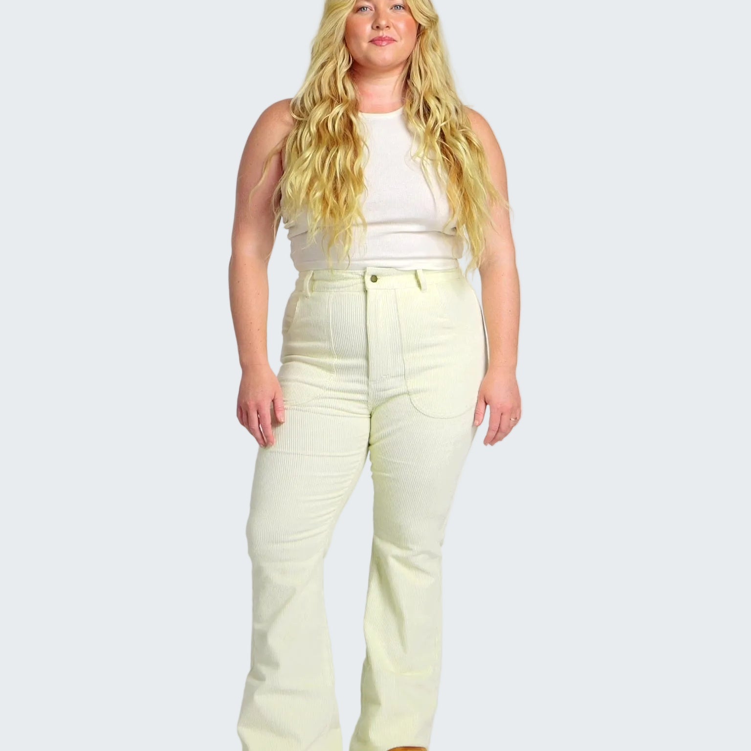 Woman wearing a white sleeveless top and light yellow pants on a white background