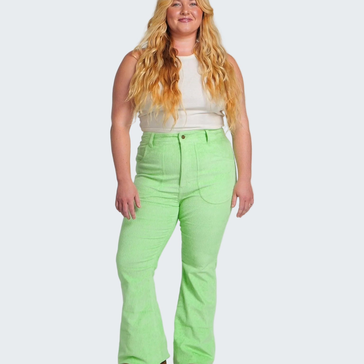 Woman wearing bright green pants and a white top on a plain background