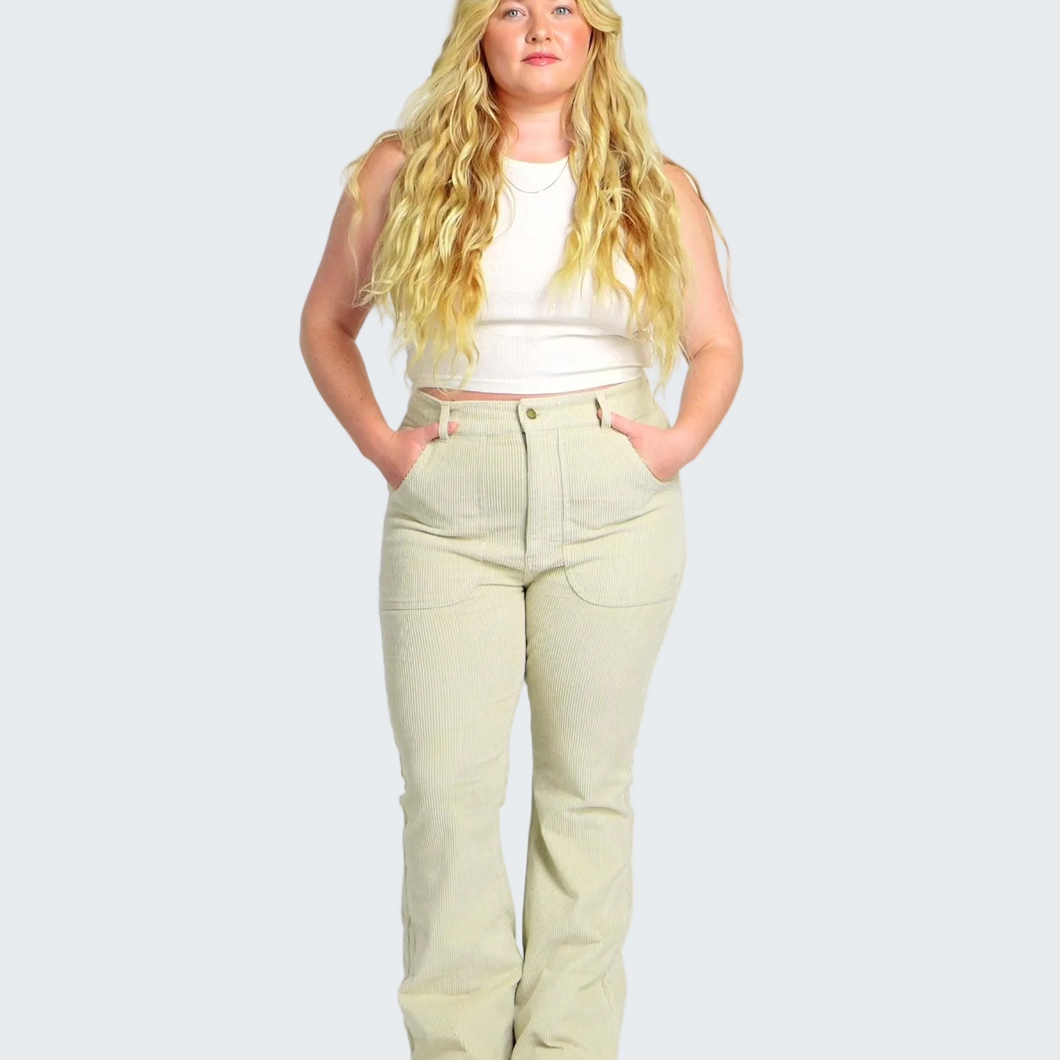 Woman wearing a white sleeveless top and light green pants on a white background