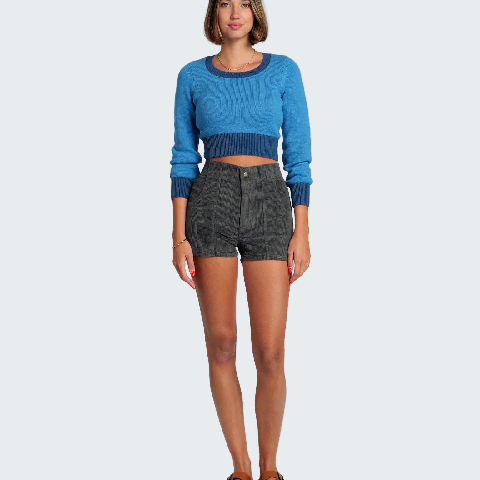 Woman wearing a blue sweater and dark shorts on a white background