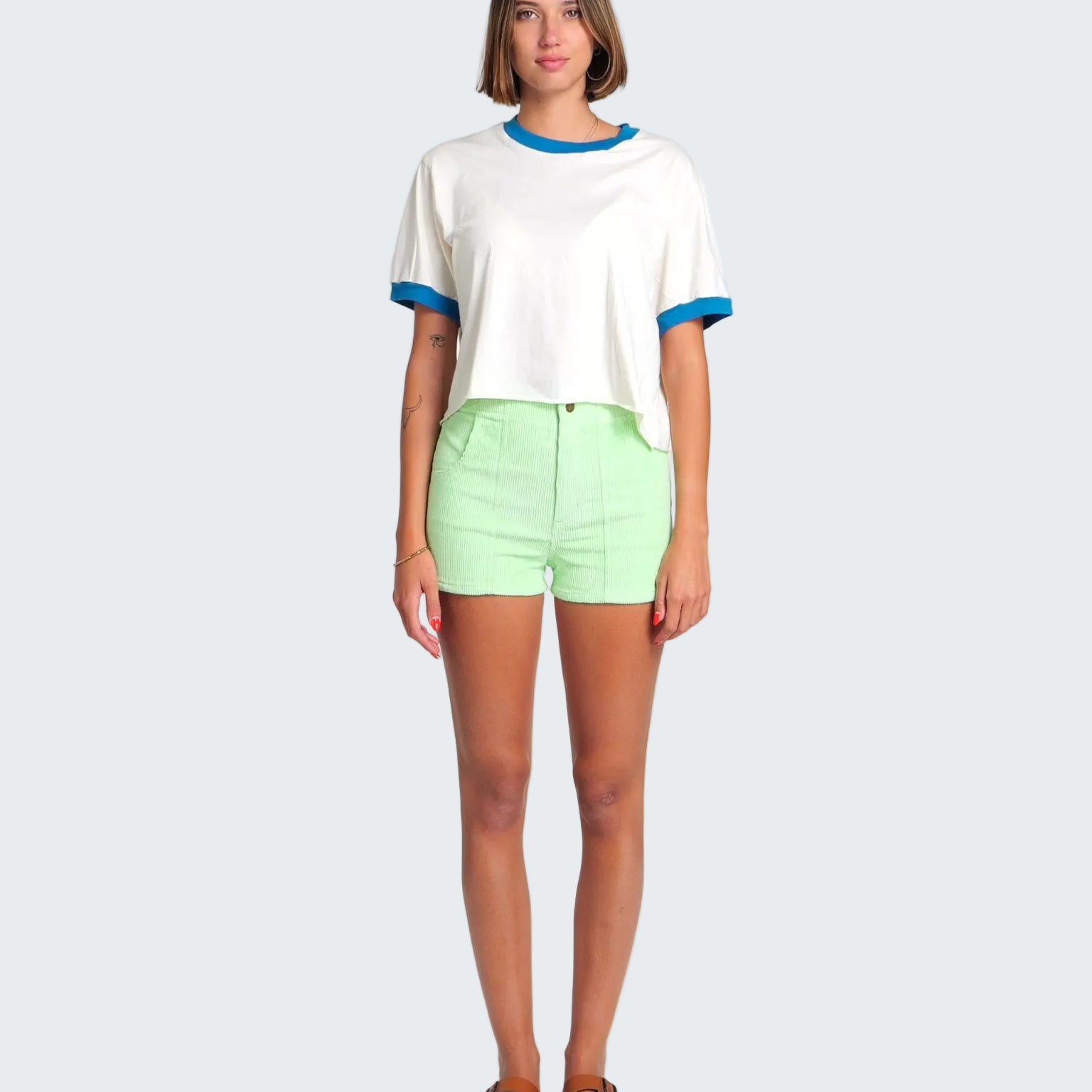 Woman wearing a white shirt with blue trim and light green shorts on a white background