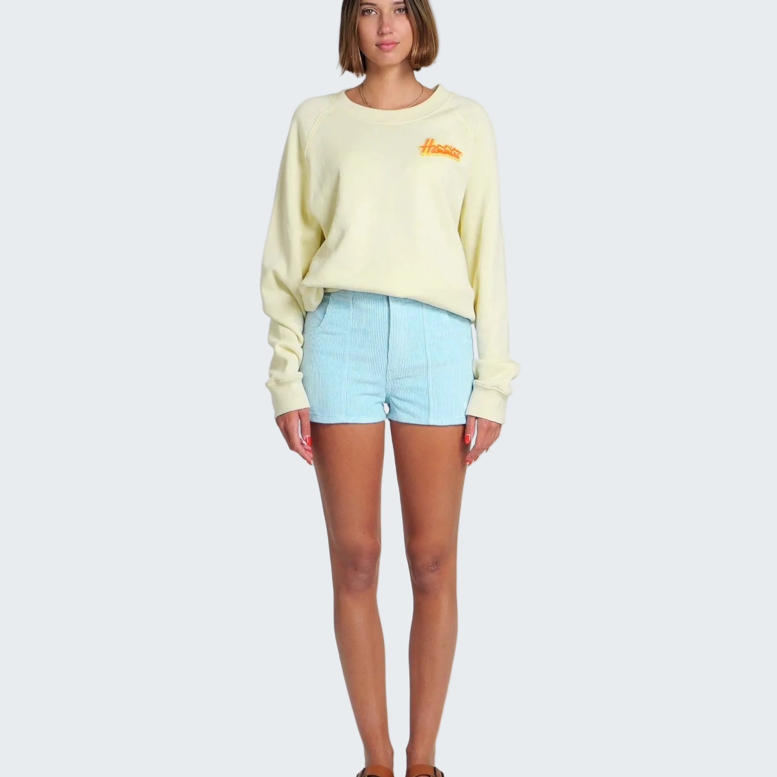 Woman wearing a light yellow sweater and light blue shorts on a white background