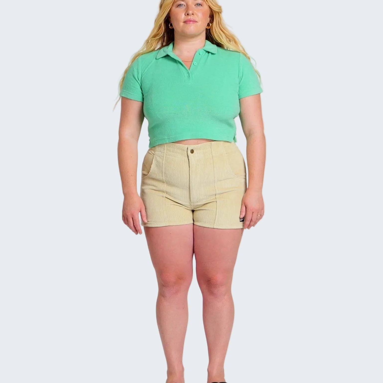Woman wearing a green polo shirt and beige shorts on a white background